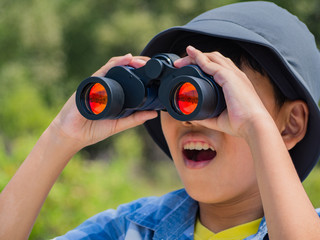 Young boy looking through binoculars on sunny summer day with happiness.