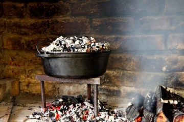 Dutch oven cooking on hot coals. Black cast iron pot on with hot coals underneath the pot and on...