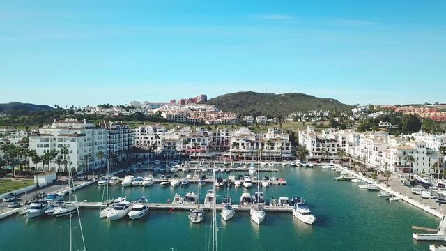 Aerial panoramic view of beautiful "Puerto de la Duquesa" in MANILVA- Malaga SPAIN. Yachts and boats docked in the Harbour. Luxury Apartment Urbanisation and Restaurants . Drone dolly in.