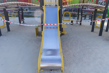 Fototapeta premium Coronavirus COVID-19 restriction. No people due to quarantine. Closed children's playground in the city. Empty park and playground. Stay at home compaign. Red warning tape on swings and slides