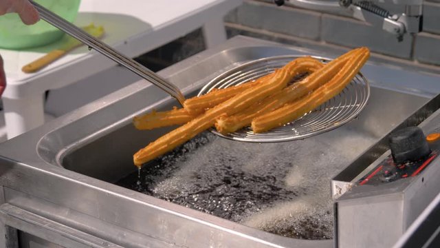 Slow motion: chef cooking homemade crunchy yellow churros in boiling oil at summer outdoor food market - close up view. Traditional spanich cuisine, catering, cookery, gastronomy, street food concept