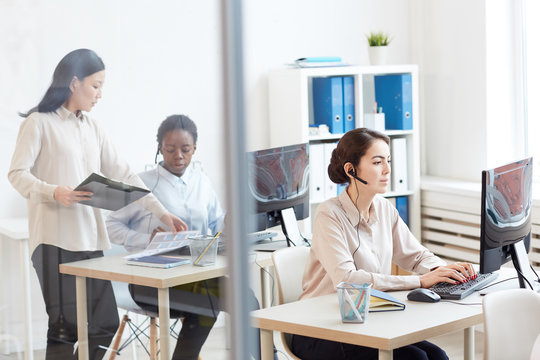 Wide angle view at call center interior with female operators wearing headsets at workplace, copy space