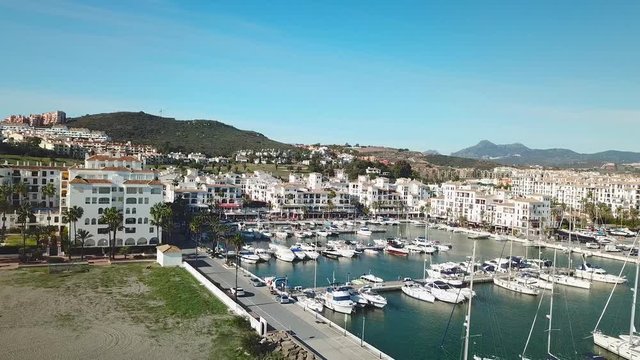 Aerial panoramic view of beautiful "Puerto de la Duquesa" in MANILVA- Malaga SPAIN. Yachts and boats docked in the Harbour. Luxury Apartment Urbanisation and Restaurants. Backward and right rotation.