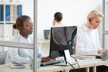 Multi-ethnic group of female call center operators using computers at workplace, focus on young...