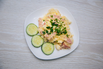 Omelet with sausage, herbs and cheese on a white plate. Dish with food on a light wooden table. Lunch fried eggs with bacon and chopped cucumber.