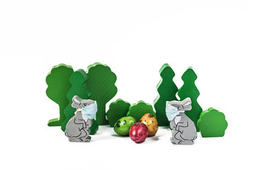 Easter bunnies in medical masks at a distance from each other.Wooden decoration with colorful eggs.Easter during a coronavirus pandemic.Social distance,self-isolation during the outbreak of Covid-19.