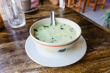 Green curry dish served in Thai restaurant in Thailand. Street food bowl of spicy soup. Foodie travel background. Asian food experience. Simple single object on wooden table.