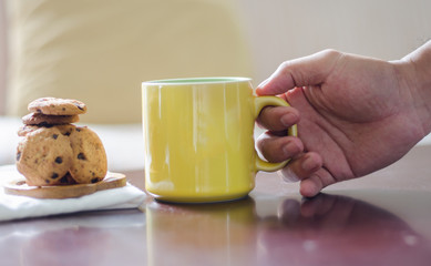 Close up of a hand holding a cup of coffee and cookies on a wooden table