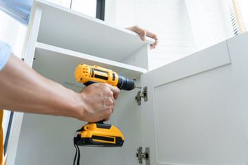 Close up portrait and details of caucasian male worker using electric screwdriver instrument in hand and repairing new wooden desk, home improvement concept.