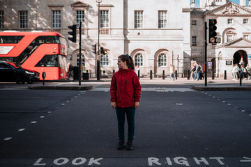 Young white girl with a red raincoat in the middle of a crosswalk in a road of London. 