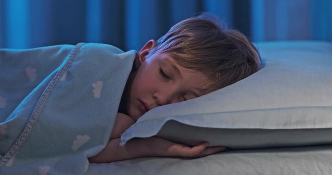 4k footage  of a sleeping child in bed.  8 years old boy sweetly sleeping in his crib. Face close-up of a sleeping child on its side. Tracking shot of a sleeping kid at midnight. Relax and resting