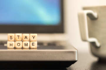Stay home is written by wooden cube letters with background of cup of coffee and laptop. home office concept