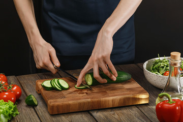 Woman cooking fresh healthy salad. Female hands cutting vegetables on board on wooden table.