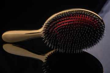 Golden hairbrush with red middle and high-quality multilayer teeth on reflective black background....