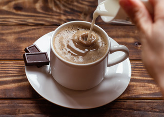 Hand holding cap of milk and pouring it to cap of coffee  on small plate with two small chocolate.   Flat Lay with no people