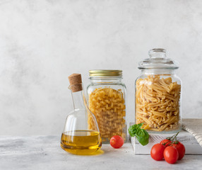 pasta in a glass jar (treccia, cellentani) and olive oil in a bottle on a gray background. Food...