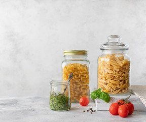 Italian pasta in a glass jar (treccia, cellentani) and fresh basil pesto. Mediterranean Kitchen. Gray background. copy space.