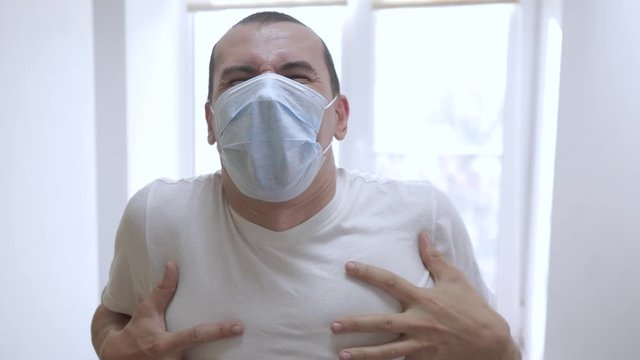 sick man in a medical mask screams in pain holds his head in his hands. concept pandemic virus lifestyle self-isolation covid 19 infection doomsday. sick dying man from infection indoors