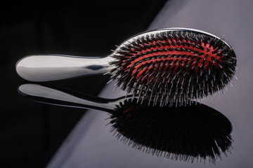 Silver hairbrush with red middle and high-quality multilayer teeth on reflective black background. subject photo. individual household item for hair calculation