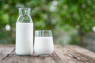 A bottle of milk and glass of milk on a wooden table on a blur background nature.