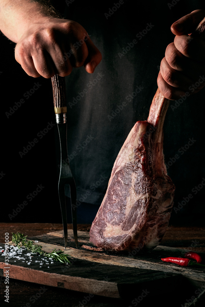 Wall mural a man holds a raw tomahawk steak on a bone of dry aged beef on a dark background