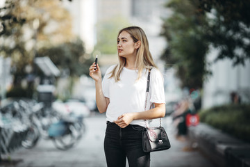 Happy blonde european girl smoke elektronic cigarette on the street