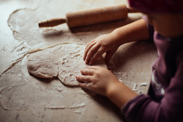 little girl's hands kneading dough on the table, side light, home cooking concept