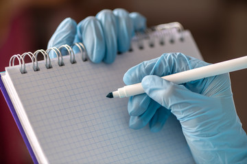 Female hand in a medical glove holds a tablet for writing and a pen