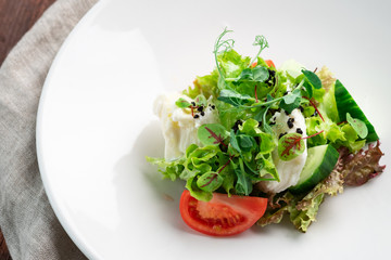 Light diet salad of mozzarella and fresh vegetables -cucumber, tomato, lettuce, peas on a white plate on a wooden background