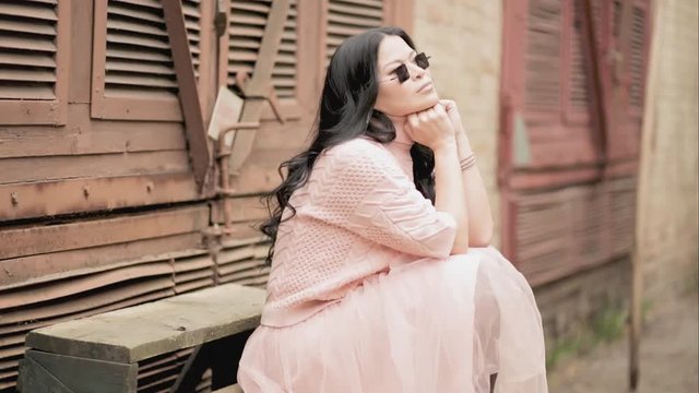 Asian woman leaned on habds sitting next to the rusty wall