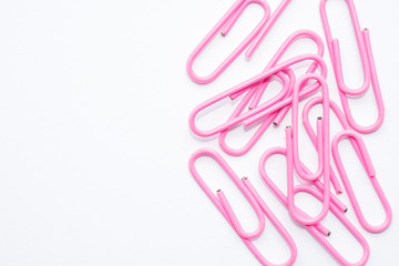 Pink paper clips on a white sheet, lying on the right side of the background, for free space for writing or text