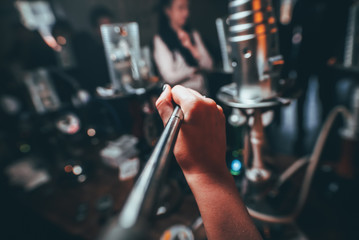 the girl smokes a hookah. Cable tube into the camera. from the first person. the background is indistinct. tightens smoke. it is a lot of hookahs.