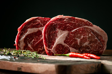 Raw rib eye beef steak with pepper and herbs on a wooden background in a butcher shop