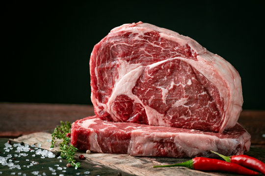 Raw rib eye beef steak with pepper and herbs on a wooden background in a butcher shop