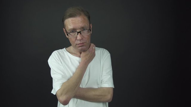 thoughtful man in t-shirt and glasses stands scratching neck
