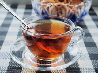 On the table there is a transparent glass Cup with tea on a glass saucer and a glass vase with bagels.