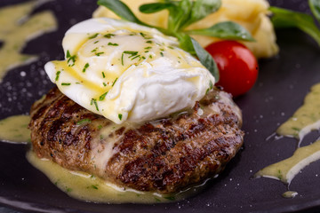 A piece of steak with egg paschot, served with puree potatoes and cherry tomatoes with greens