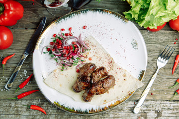  Restaurant dish on a wooden background with vegetables. Azerbaijani pork kidneys with onions on...
