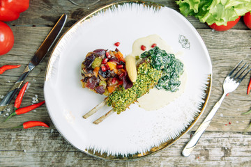 Restaurant dish on a wooden background with vegetables. Lamb ribs in spices and sauce on a plate.