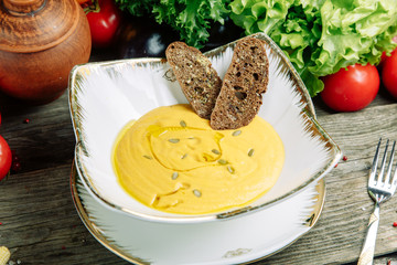 Restaurant dish with vegetable decor on a wooden background. Puree soup with mushrooms and sour cream on a plate.