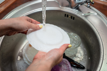 Woman washing dishes in kitchen sink, closeup view. Cleaning chores