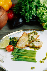 Restaurant dish with vegetable decor on a wooden background. Sea fish fried on a plate with sauce.