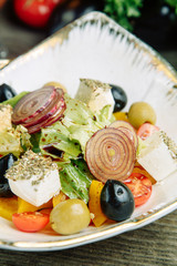 Restaurant dish on a wooden background with vegetables. Greek salad with feta cheese and spices on a plate.