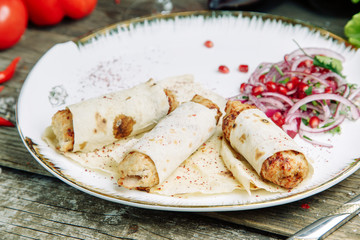 Restaurant dish on a wooden background with vegetables. Lula kebab in lavash with pomegranate and onion on a plate.