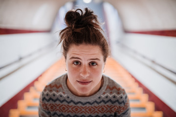 Portrait of a young woman dressed in a pastel colored woolen sweater and her hair up, climbing the subway stairs.