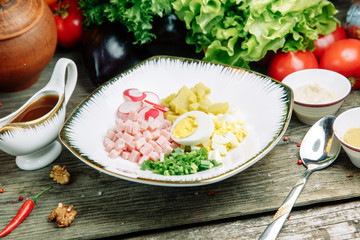 Restaurant dish on a wooden background with vegetables. Okroshka salad with kvass and horseradish on a plate.