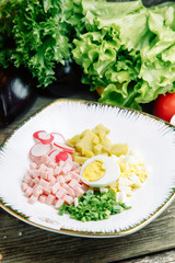 Restaurant dish on a wooden background with vegetables. Okroshka salad with kvass and horseradish on a plate.