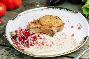 Restaurant dish on a wooden background with vegetables. Pork on the bone with sauce and garnish on a plate in pita bread.