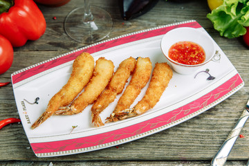 Restaurant dish on a wooden background with vegetables. Prawns in tempura with sweet and sour sauce on a plate.