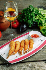 Restaurant dish on a wooden background with vegetables. Prawns in tempura with sweet and sour sauce on a plate.